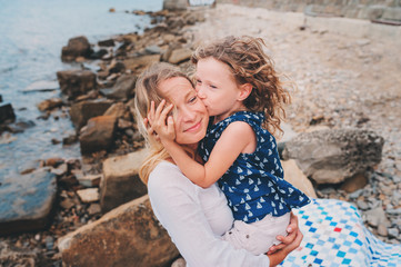 portrait of happy mother and daughter spending time together on the beach on summer vacation. Happy family traveling, cozy mood. Child kissing mother.