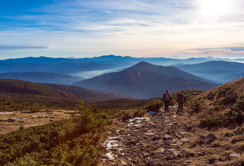 Two Hikers walking on Mountain Path Sunset Mountains Background
