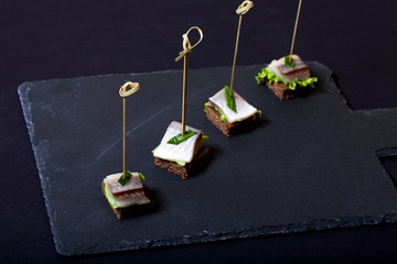 Small snacks canape with herring, rye bread, lettuce and green o