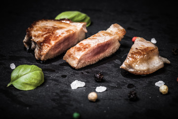 Fried meat with herbs and spices on a black slate plate. Selecti