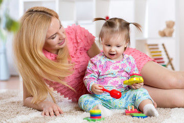 Baby playing with her mother on carpet in nursery