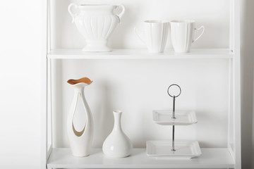 Fototapeta na wymiar Clean dishes and vases on white wooden shelf