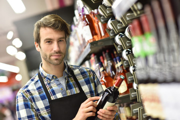 Wine specialist putting bottle up in winery section of supermarket