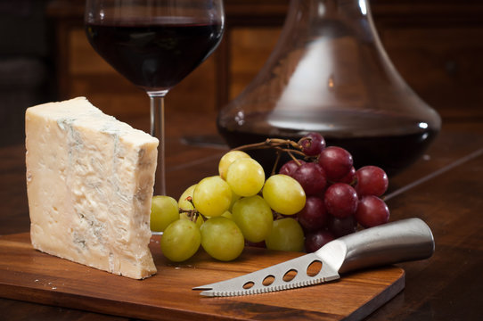 Glass of red wine served from an elegant decanter with fresh gorgonzola cheese and red and green grapes.