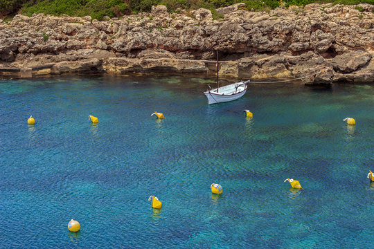 Lonely mediterranean llaut boat anchored in turquoise water of a cove at Menorca, Balearic islands