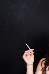 Woman's Hand Holding a Smoking Cigarette isolated on Black Background. Close up with White Cigarette Smoke. Copy Space for Text or Image
