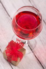 Gift box and glass of rose wine on wooden background. Selective focus