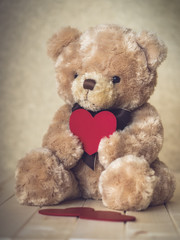 Toy bear with the heart in its hands on the wooden floor