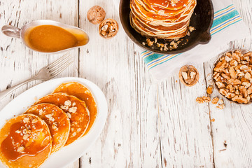 Pancakes with caramel and nuts on an old wooden background.