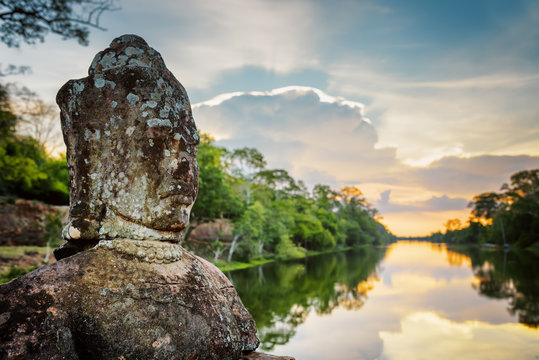 Mossy stone face Asura and sunset over moat. Angkor, Cambodia