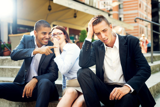 Gossip people in front of their office sitting on stairs,depressed businessman portrait and gossip out of focus in background.