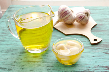 Fresh sliced garlic in glass bowl and oil in glass bottle, on wooden background