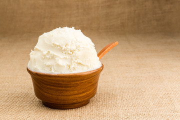Shea butter in the wooden bowl on the jute fabric background.