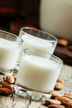 Almond milk in small glasses and spilled dry almonds on old wood