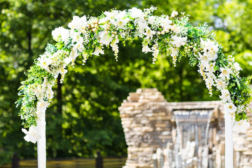 Beautiful white wedding arch decorated with white flowers outdoors