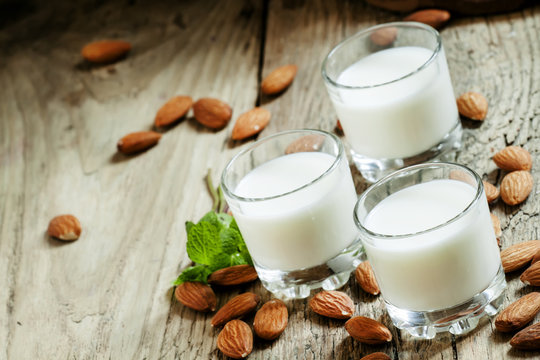 Almond milk in small glasses and spilled dry almonds on old wood