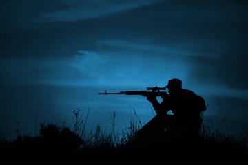 Silhouette of military sniper with weapons at night.