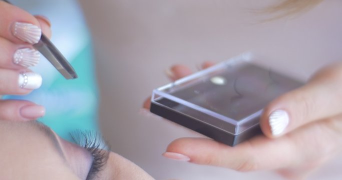 Beautician Female Stylist is Putting a Rhinestones to Model's Lashes by Pincet Close Up Applying a Makeup for a Woman Model New Makeup Beauty Salon