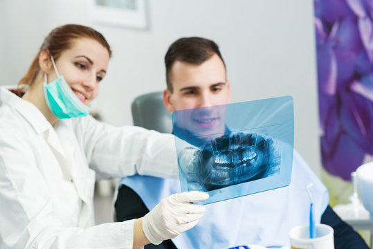 Doctor and patient looking at roentgen of human jaw, focus is on roentgen. Dentist office.