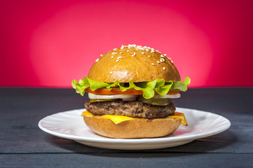 Appetizing hamburger with vegetables on white plate on wooden table. Fast food, junk food.