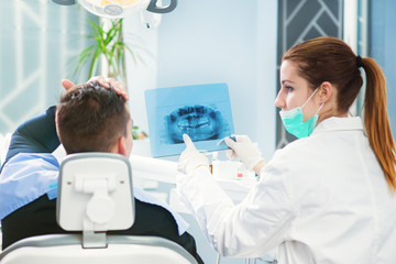 Doctor and patient looking at roentgen of human jaw. Patient is holding his head. Dentist office.