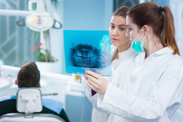 Dentist looking at roentgen of human jaw. Consulting. Patient blurred on chair in background.