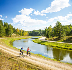Young Happy Couple Riding Bicycles by the River - 101842303