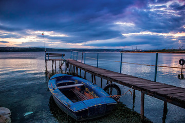 Obraz premium Boat at wooden pier with bench on a lake with stormy sky