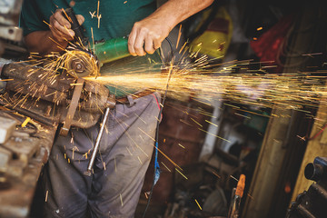 Craftsman sawing metal with disk grinder in workshop. Shallow depth of field.