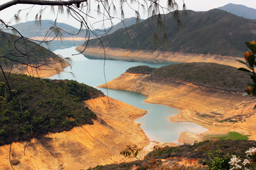 Hong Kong high island water reservoir running dry. Low water levels expose bright orange soil on...