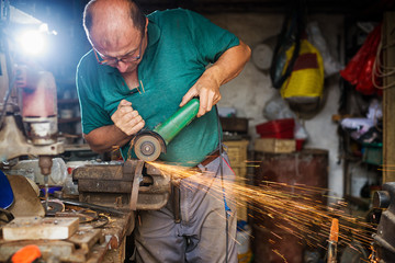 Craftsman sawing metal with disk grinder in workshop. Shallow depth of field.