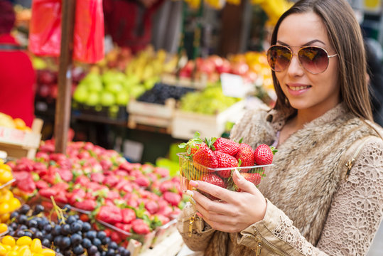 Beautiful young woman holding fresh strawberries at marketplace.