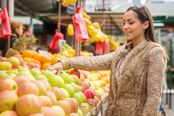 Beautiful female choosing fresh apples ready for sale at marketplace. Shallow depth of field.