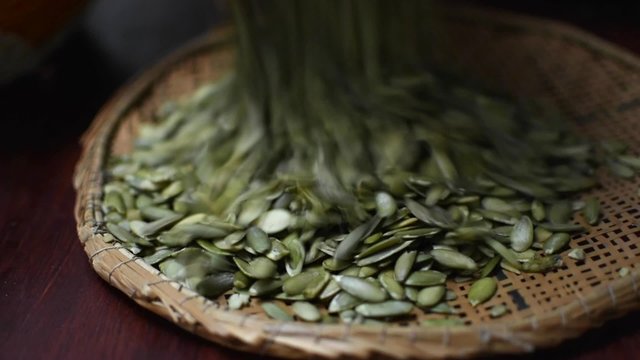 Closeup traditional reed sifter used to dump pile of fresh green pepitas pumpkin seeds on table