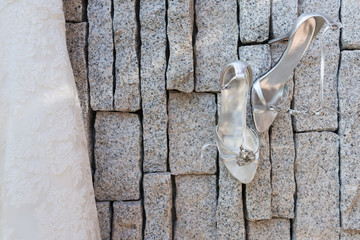 Silver bridal shoes hanging on granite with part of bride dress beside.
