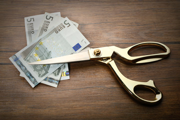 Golden scissors cut money on wooden background