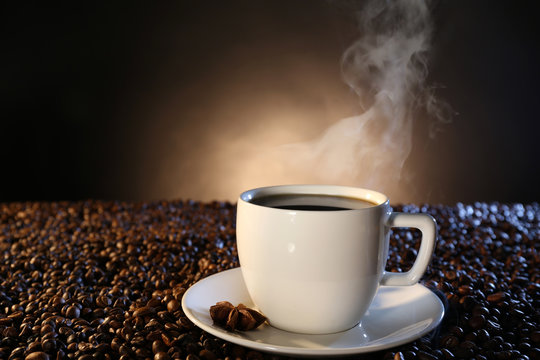 Cup of hot coffee among coffee beans on dark background