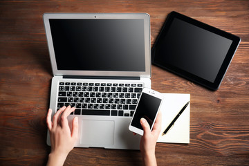 Modern tablet, mobile phone, and female hands using laptop, on the wooden background