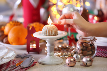 Woman hand lights a candle on holiday table setting