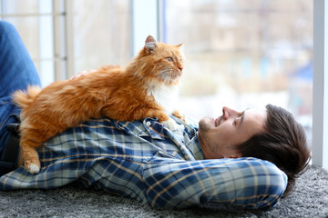Young man with fluffy cat lying on a carpet