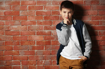 Cute little boy standing near brick wall, close up