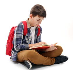 Cute little boy with red backpack reading a book, isolated on white