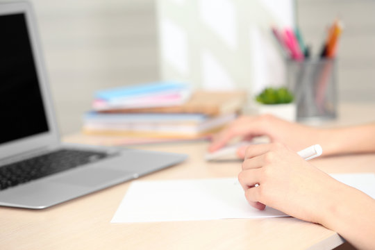 Woman making notes on a sheet of paper with a laptop beside