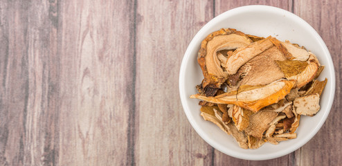 Dried porcini mushroom in a white bowl over wooden background