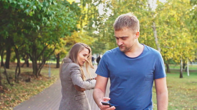 Man walking in the park and looking at his smartphone while woman bumping into him 