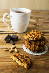 Chocolate icing cookies with peanuts and tea on a rustic wooden table, vertical. Breakfast biscuits and tea.