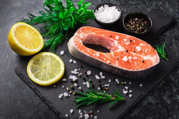 Raw salmon steak with salt, lemon and herb on the dark background