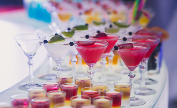 Beautiful row line of different colored alcohol cocktails with mint on a christmas party, martini, vodka,and others on decorated catering bouquet table on open air event, picture with beautiful bokeh