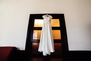 Beautiful wedding dress hanging on a door. Bridal morning.