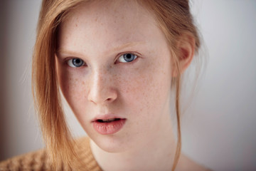 Naklejka premium Portrait of beautiful pensive girl with red hair at home. Cute redhead and freckles woman face closeup portrait with healthy skin.